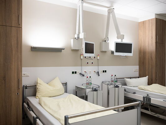 Krankenhauszimmer mit zwei Betten, Monitore und medizinische Geräte an der Wand.