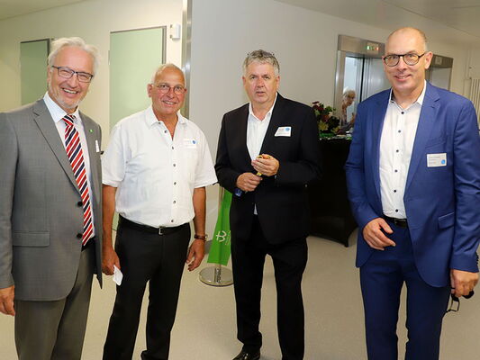 Vier Männer in Anzügen bei einer Veranstaltung, lächelnd und in einer modernen Umgebung stehend.