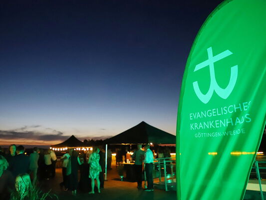 Leute bei einer abendlichen Veranstaltung mit einem Banner des Evangelischen Krankenhauses Göttingen-Weende.