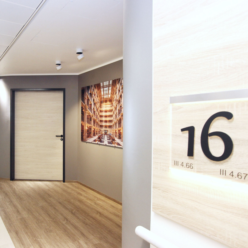 Flur mit Holztür, Wandbild einer Bibliothek und Zimmernummer 16.