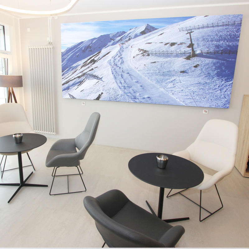Moderne Lounge mit Sesseln, Tischen und großem Winterlandschaftsbild an der Wand.