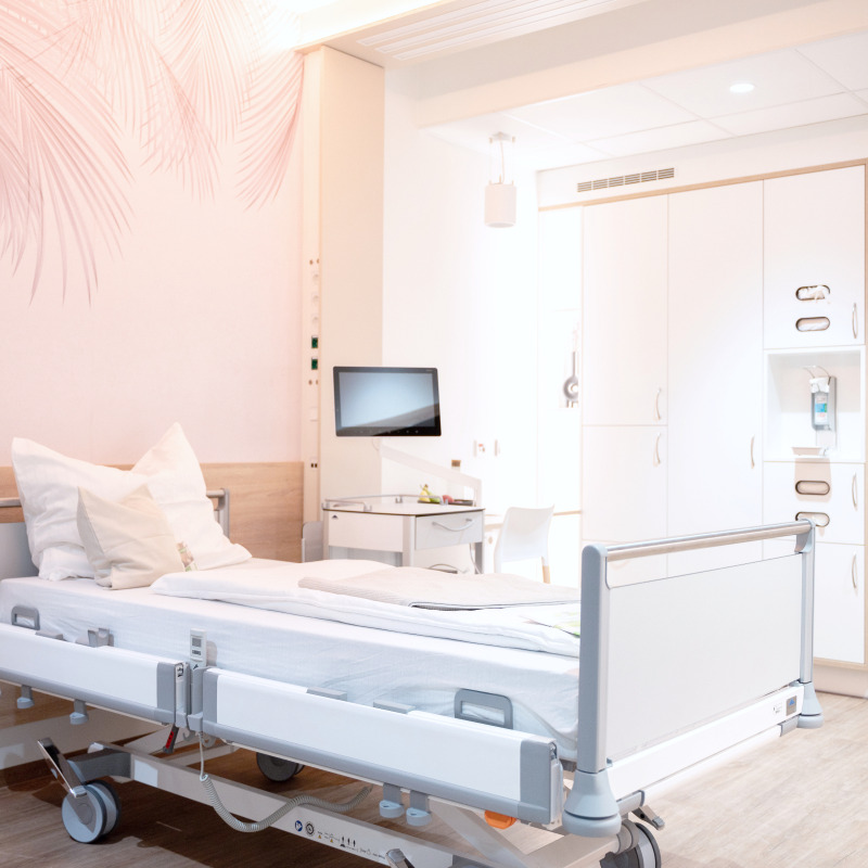 Ein modernes Krankenhauszimmer mit Bett, Monitor, Schrank und hellen Wänden.