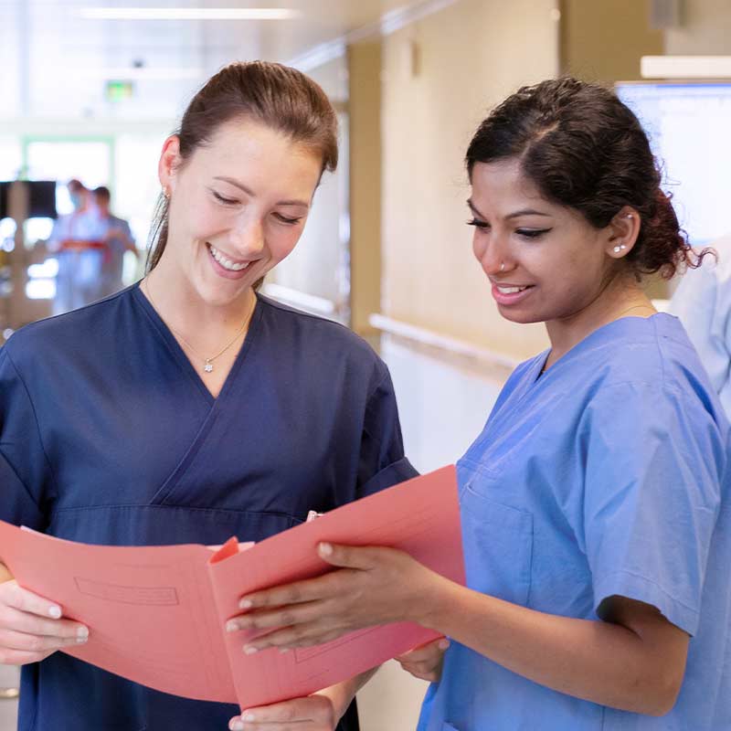 Zwei Krankenschwestern lesen gemeinsam Dokumente in einem Krankenhausflur.