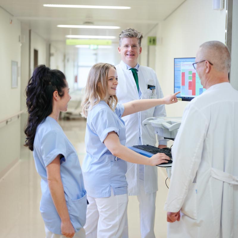Medizinisches Team in einem Krankenhausflur, bespricht Daten auf einem Computerbildschirm.