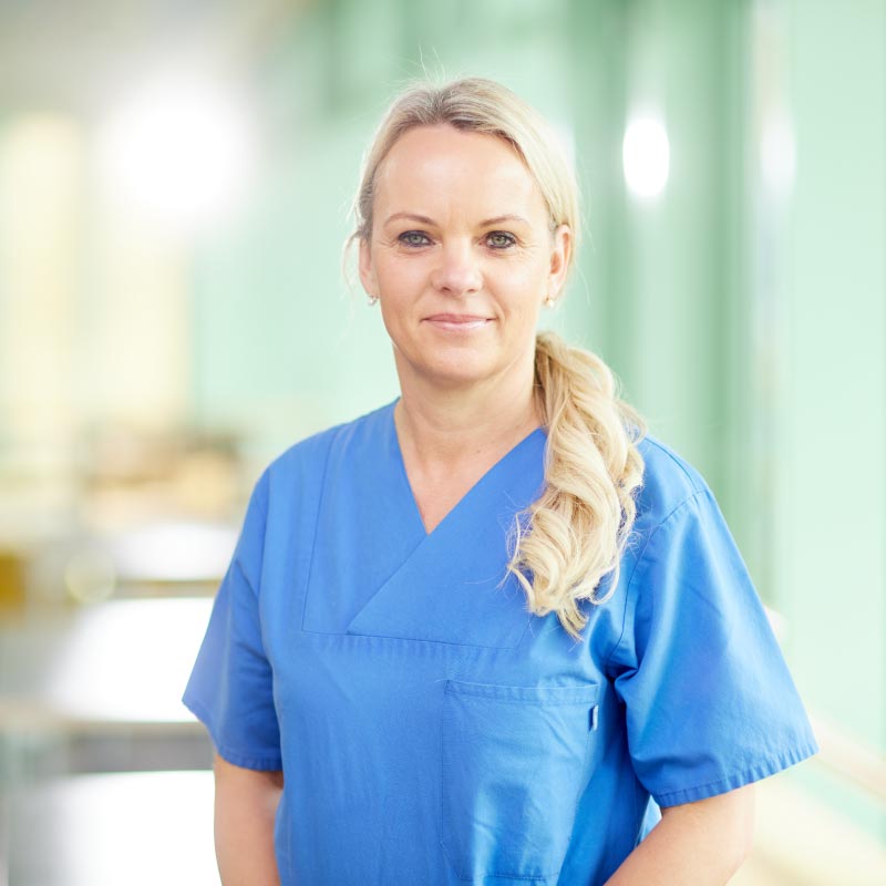 Eine Person in blauer medizinischer Kleidung steht in einem hellen Raum.