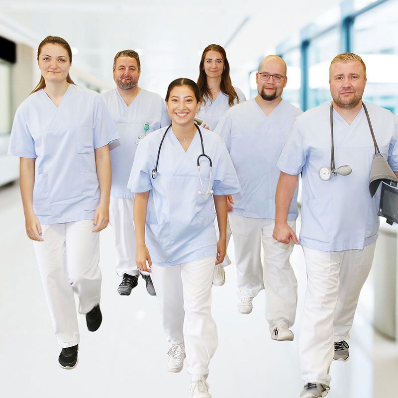 Eine Gruppe von medizinischem Personal in blauen Kitteln geht lächelnd durch einen Krankenhausflur.