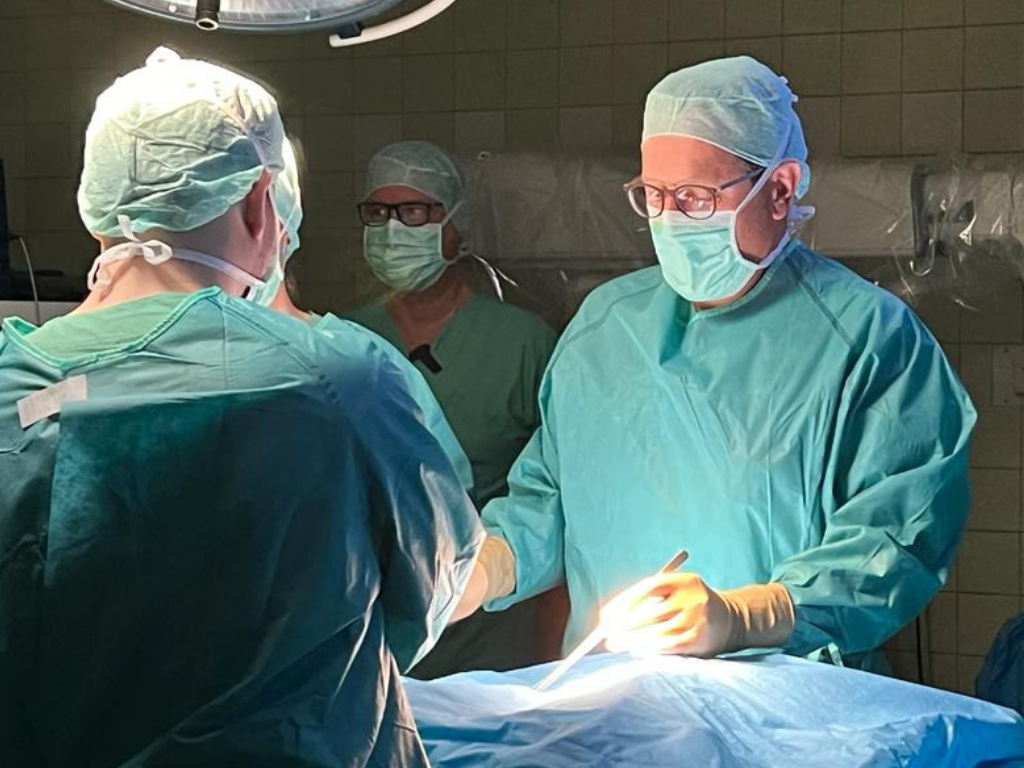 . Chirurgen im OP führen eine Operation durch, gekleidet in sterile Kleidung mit OP-Masken und Handschuhen.