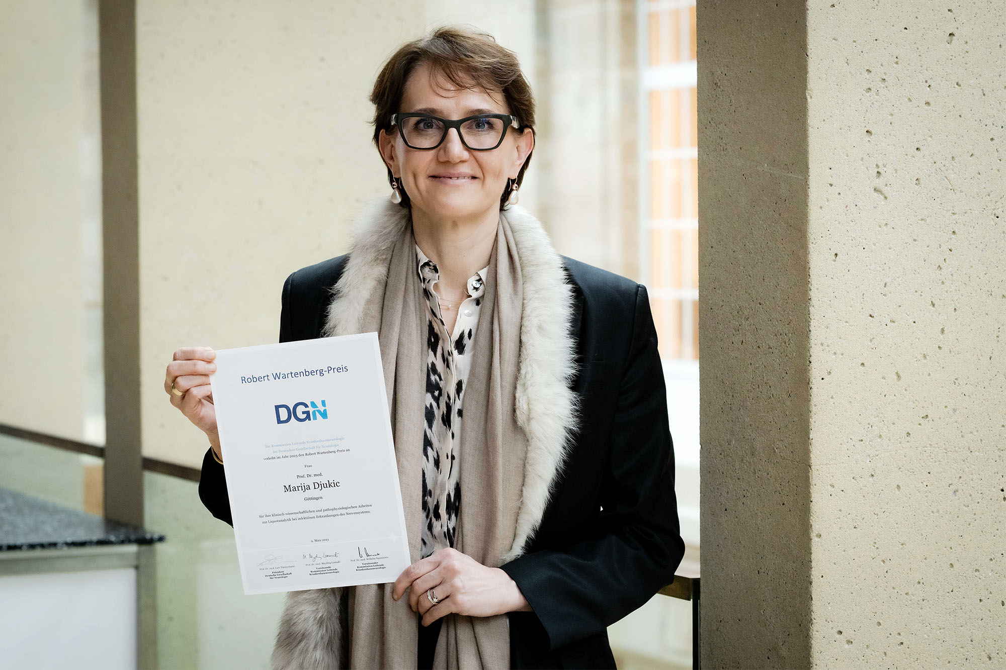 Eine Person hält eine Urkunde mit der Aufschrift "Robert Wartenberg-Preis" der DGN.