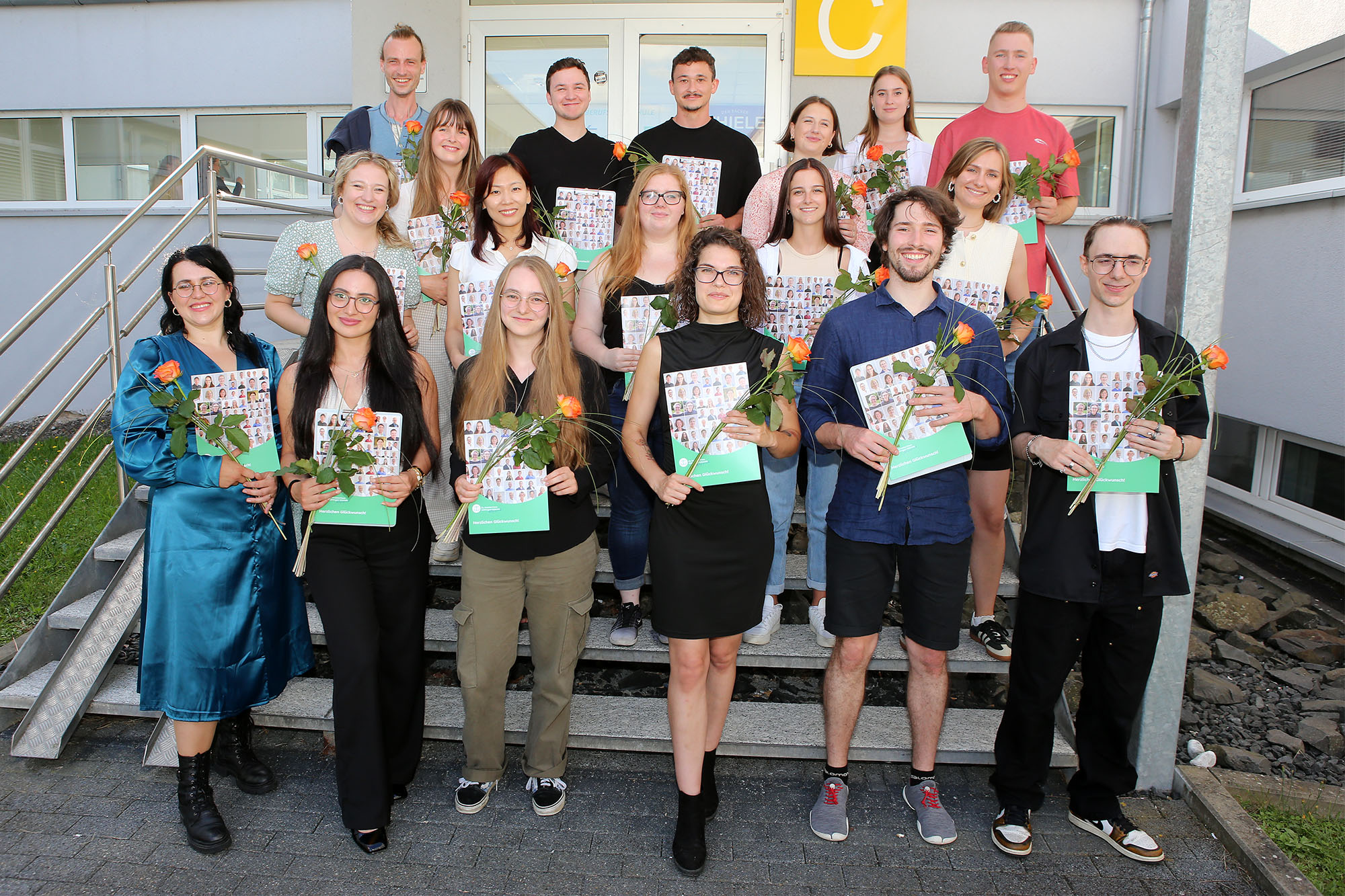 Gruppe von Menschen, die Zertifikate halten, posiert auf einer Treppe, einige halten Rosen.