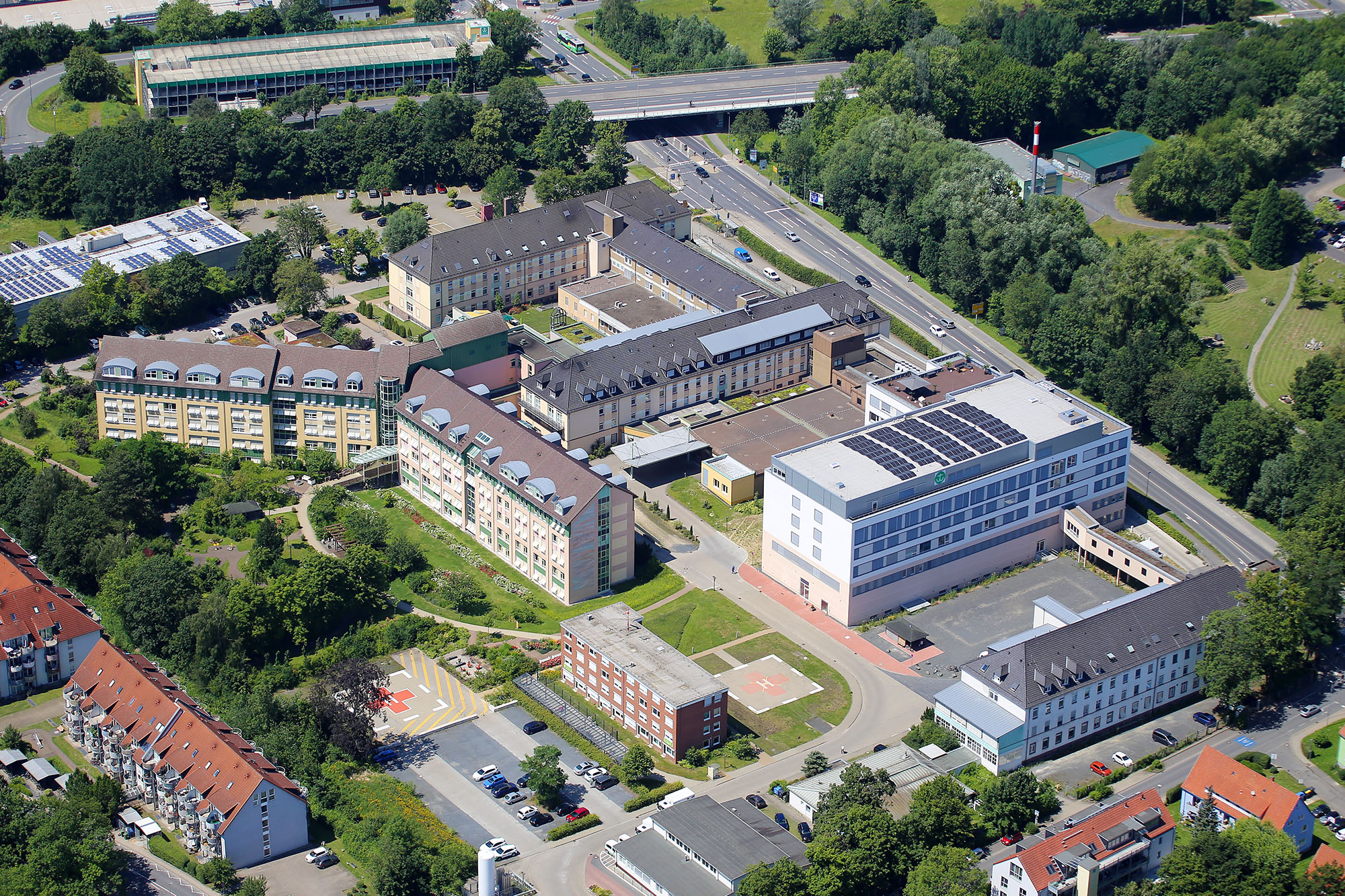 Luftaufnahme eines Krankenhauskomplexes mit mehreren Gebäuden, Helipad und umgebender Vegetation.