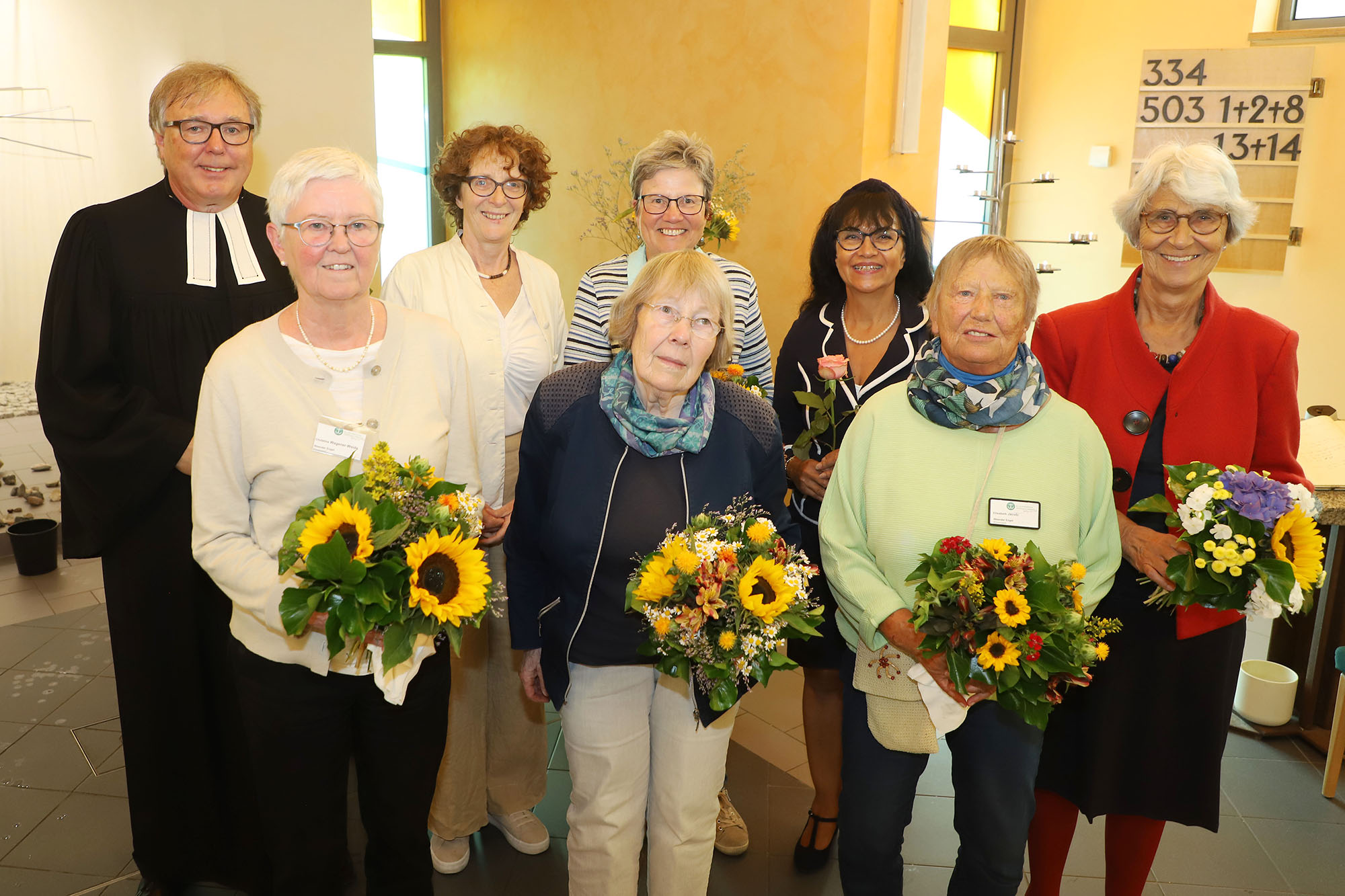 Eine Gruppe von älteren Menschen mit Blumensträußen posiert für ein Foto, eine Person trägt einen Talar.