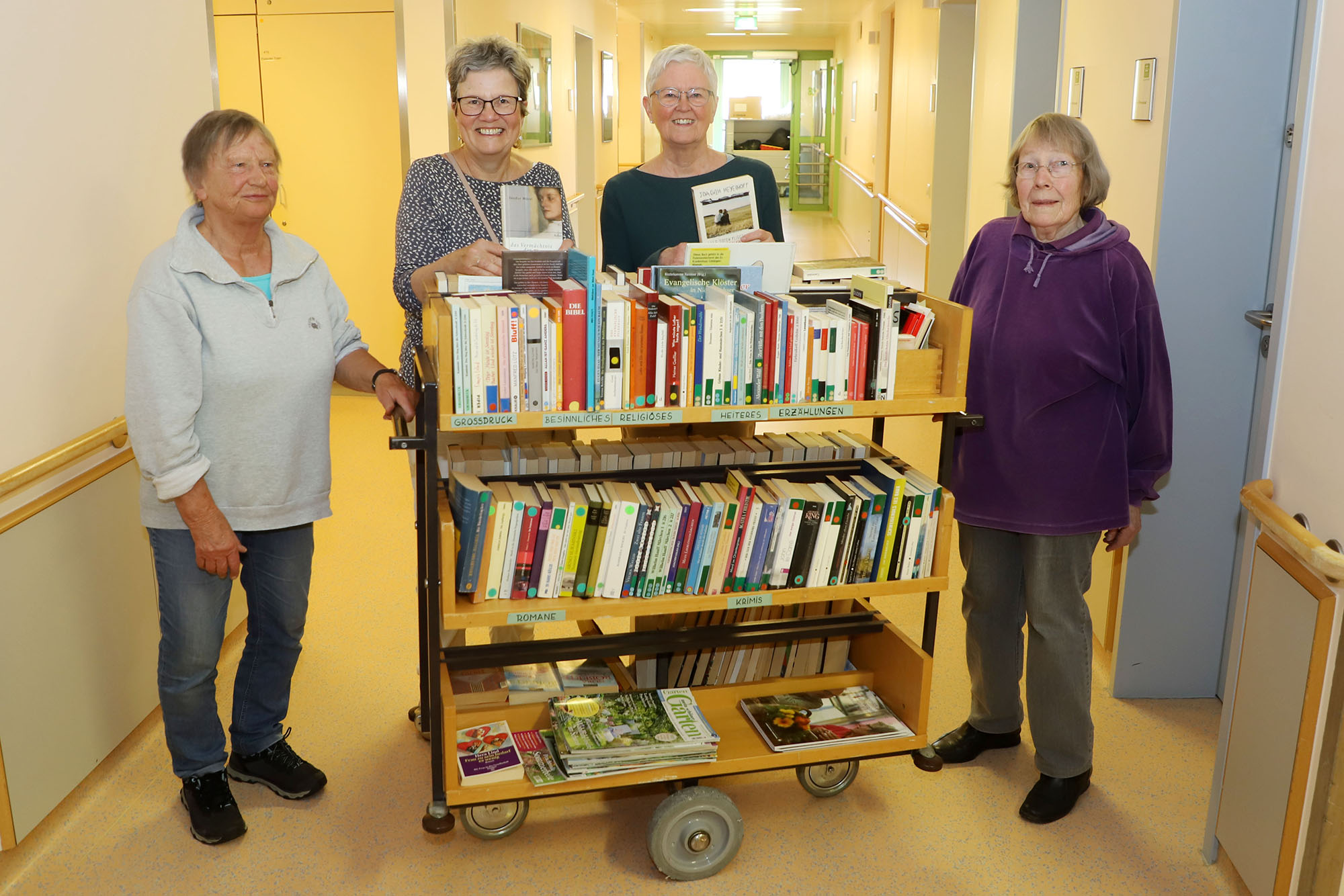 Vier Personen stehen um einen Bücherwagen in einem Flur herum.