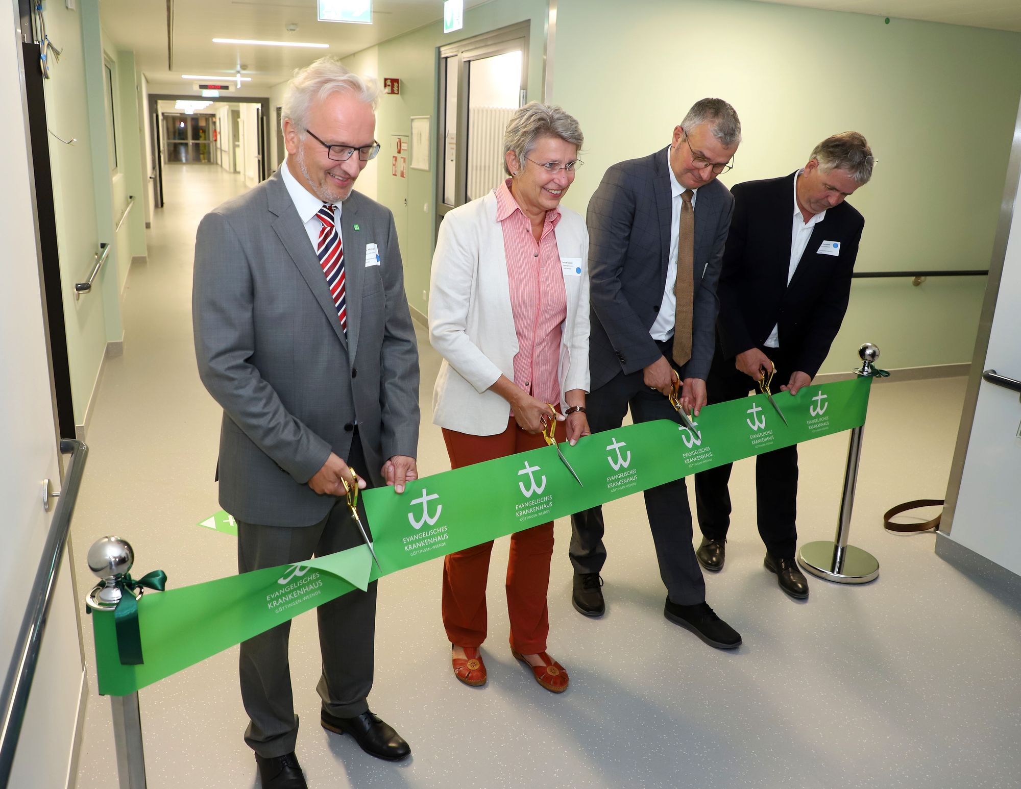 Vier Personen schneiden ein grünes Band im Krankenhausflur durch.