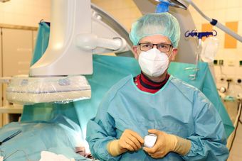 Ein Chirurg in OP-Kleidung hält ein medizinisches Gerät, umgeben von Krankenhausausrüstung.