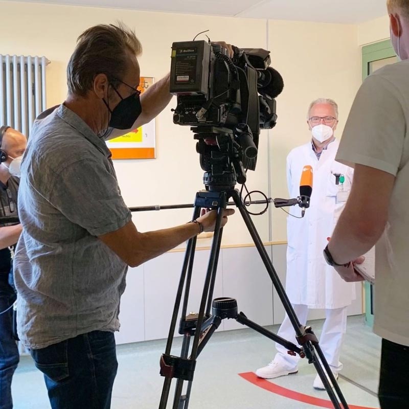 Ein Arzt wird von einem Kamerateam in einem Krankenhaus interviewt.