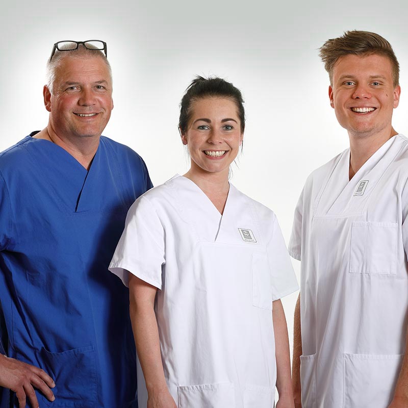 Drei Personen in medizinischer Kleidung lächeln in die Kamera.