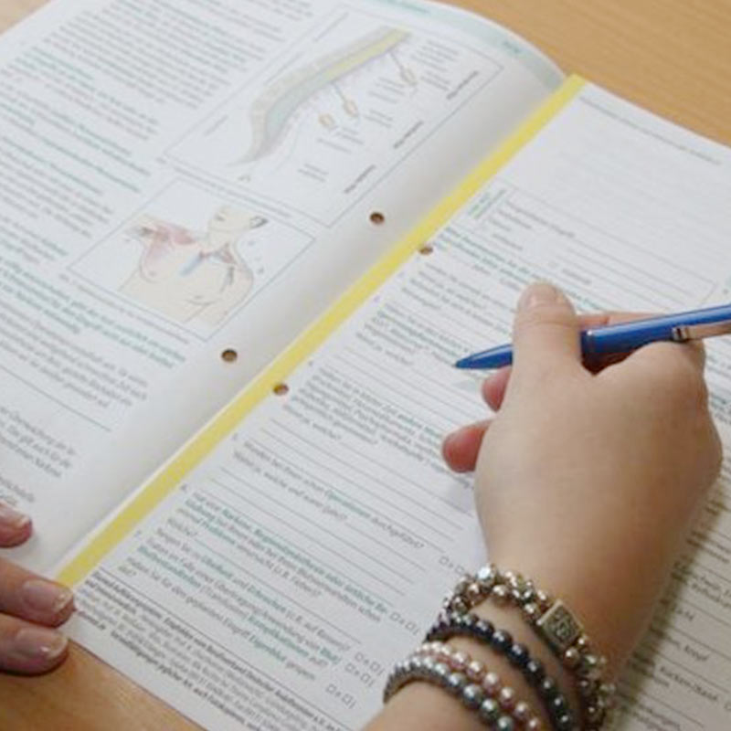 Eine Person macht Notizen in einem offenen Buch mit medizinischen Diagrammen.