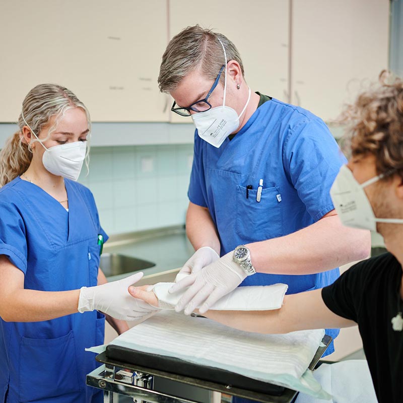 Gesundheitspersonal legt einem Patienten mit Maske einen Verband an.