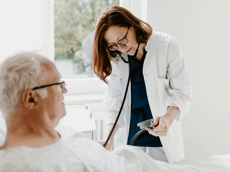 Ein Arzt untersucht einen älteren Mann im Krankenbett mit einem Stethoskop.