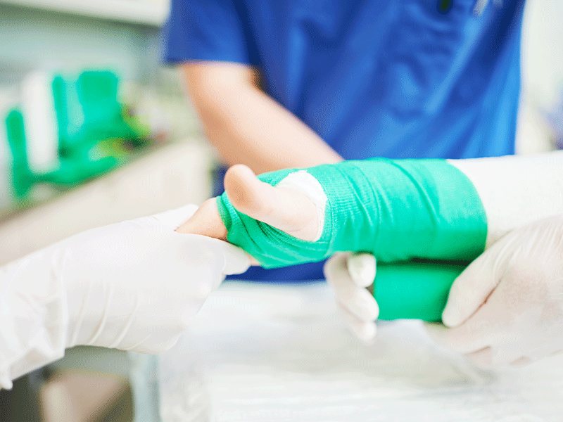 Ein Arzt verbindet die Hand eines Patienten mit einem grünen Verband.