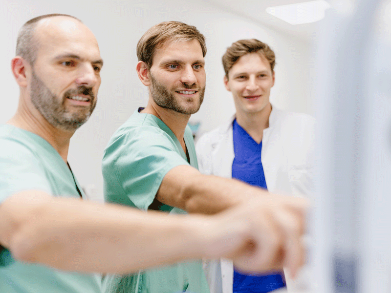 Drei Männer in medizinischer Kleidung schauen auf etwas, diskutieren oder analysieren es gemeinsam.