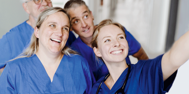 Vier lächelnde Personen in blauer medizinischer Kleidung machen ein Selfie.