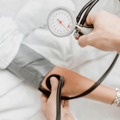 Eine Person misst mit einem Blutdruckmessgerät den Blutdruck eines Patienten im Bett.