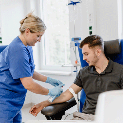 Eine Krankenschwester bereitet eine Blutabnahme bei einem sitzenden Mann vor.