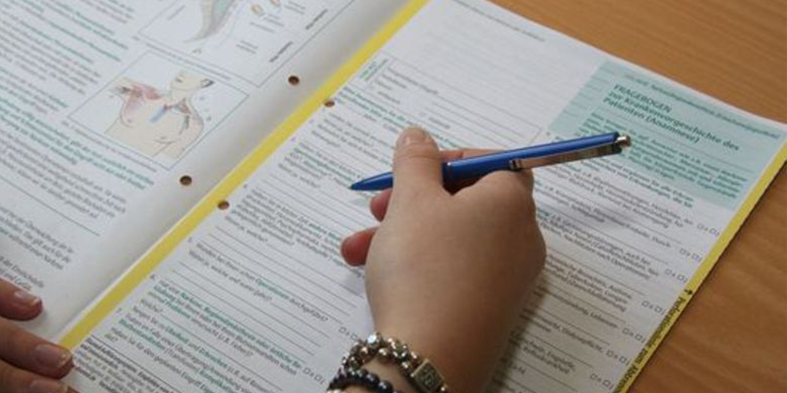 Eine Hand hält einen Stift über ein Formular mit medizinischen Diagrammen und Texten, das auf dem Tisch liegt.