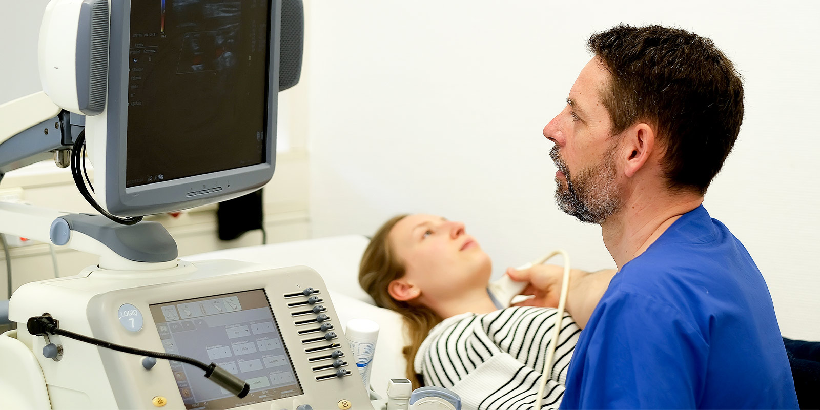 Ein Arzt führt bei einer liegenden Patientin einen Ultraschall durch.