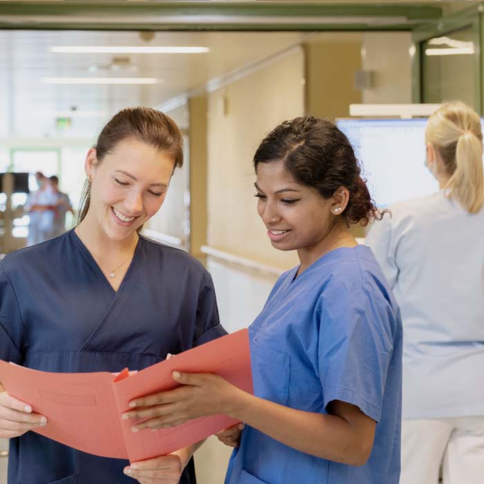 Zwei Krankenschwestern schauen sich in einem Flur gemeinsam ein Dokument an.