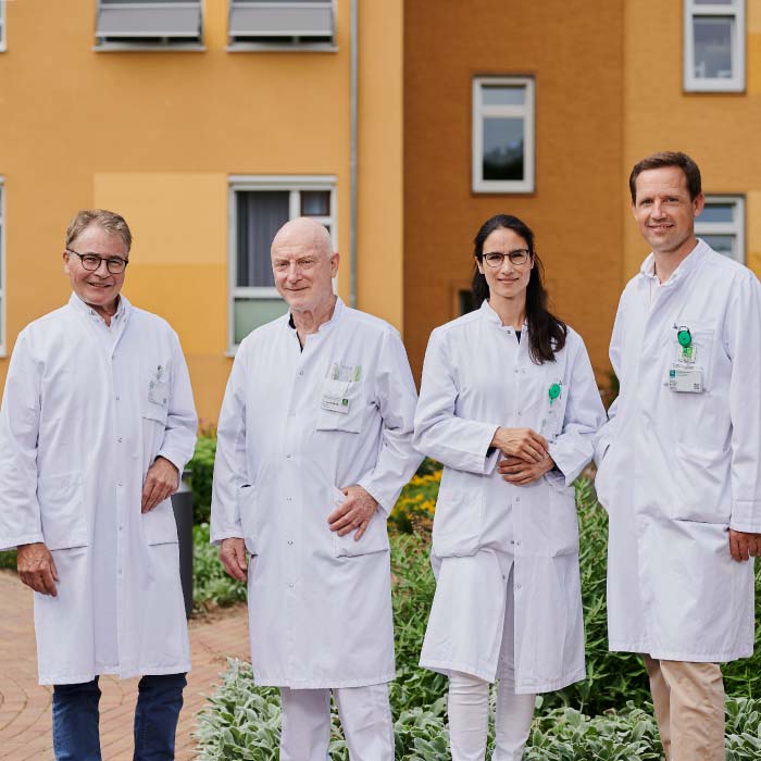 Vier Ärzte in weißen Kitteln stehen vor einem Gebäude.