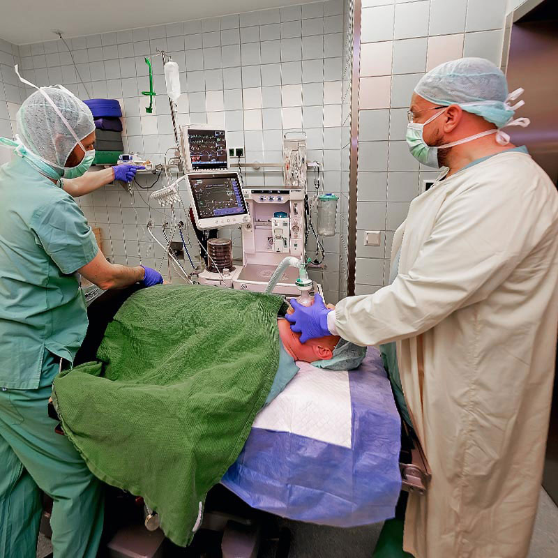 Ärzte bereiten Patienten im OP-Raum vor, mit Überwachungsmonitor und Beatmung.