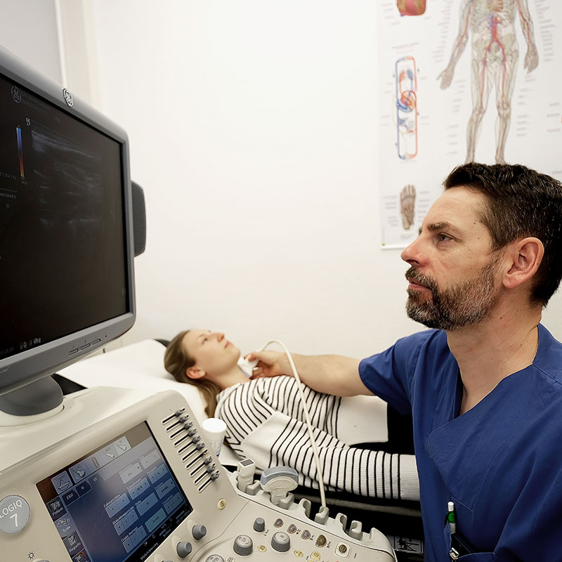 Ein Arzt führt bei einer Frau einen Ultraschall durch, Gerätebildschirm sichtbar.