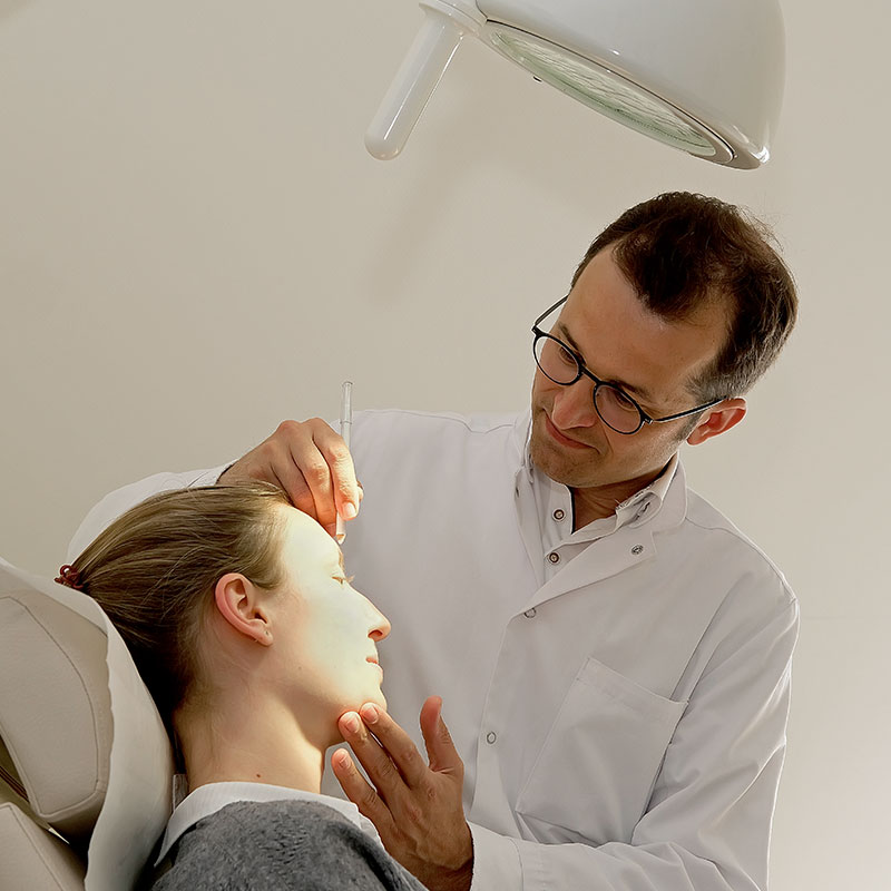 Ein Arzt injiziert einem Patienten eine Spritze ins Gesicht, während er in einer Klinik sitzt.