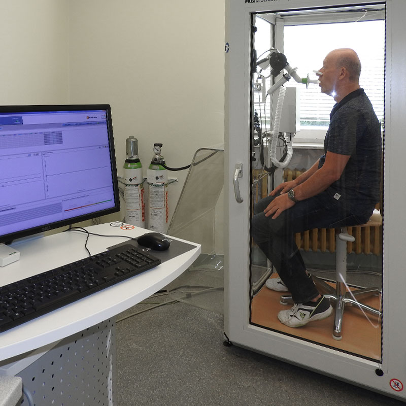 Ein Mann sitzt in einer Kabine für einen Lungenfunktionstest. Ein Computer überwacht die Ergebnisse auf einem Bildschirm.