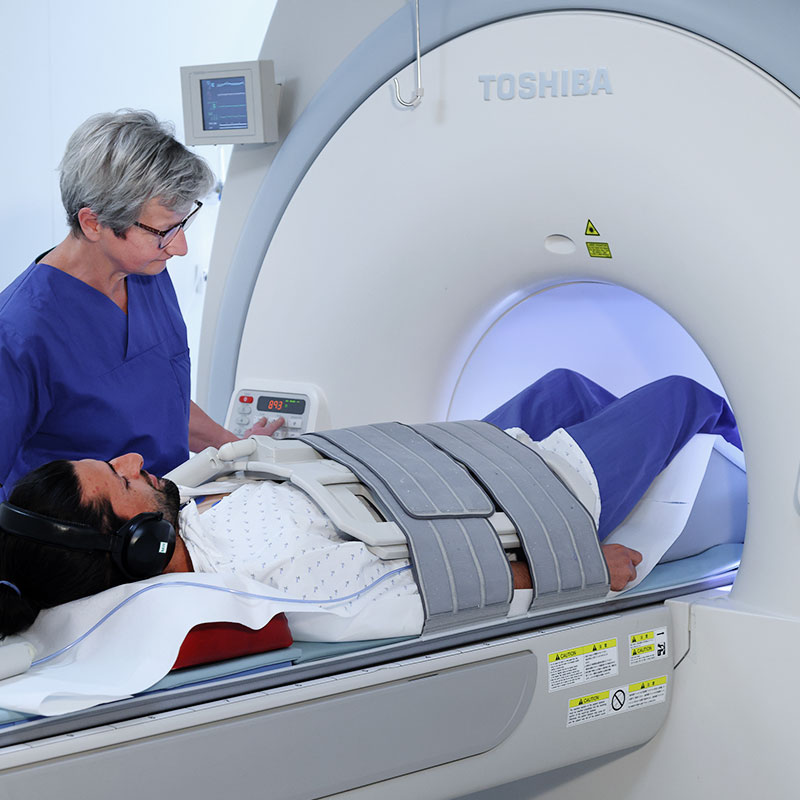 Ein Patient liegt in einem MRT-Scanner, betreut von medizinischem Personal in blauer Kleidung.