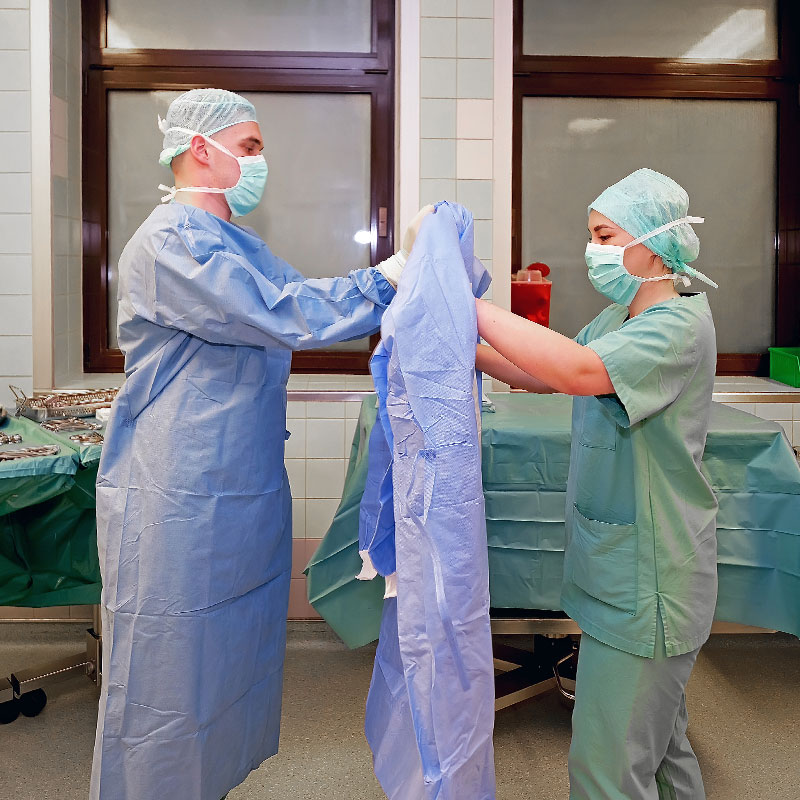 Medizinisches Personal im OP, das sterile Kittel anzieht.