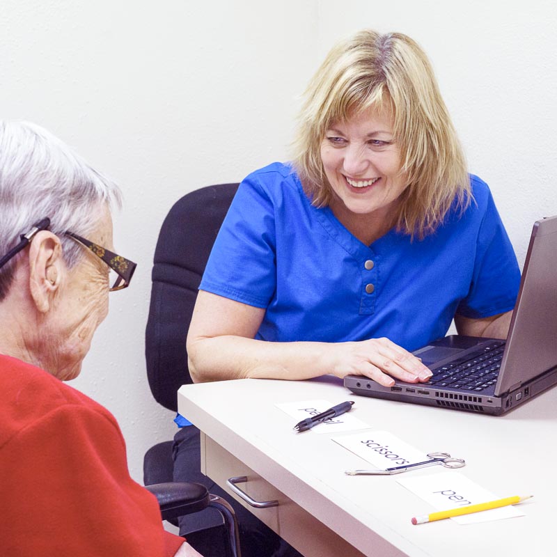 Zwei Frauen in einem Gespräch an einem Tisch mit Laptop, Stiften und Karten. Eine Frau trägt blau, die andere rot.