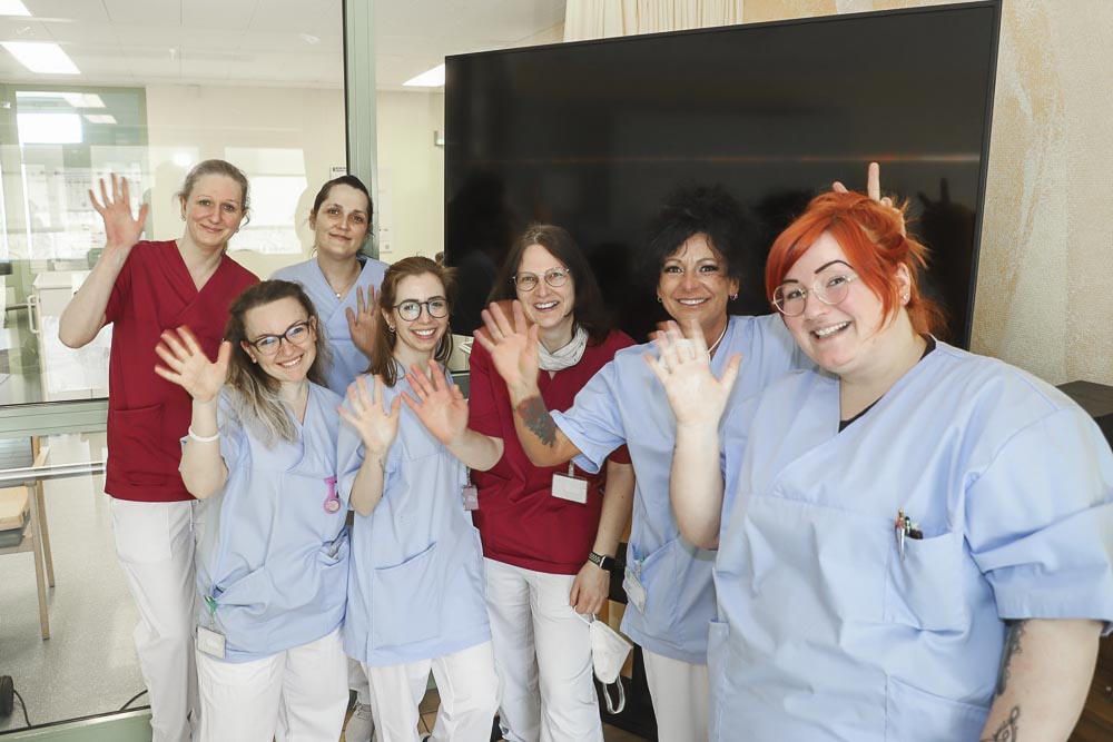 Eine Gruppe von Krankenschwestern in Uniformen winkt lächelnd in die Kamera.