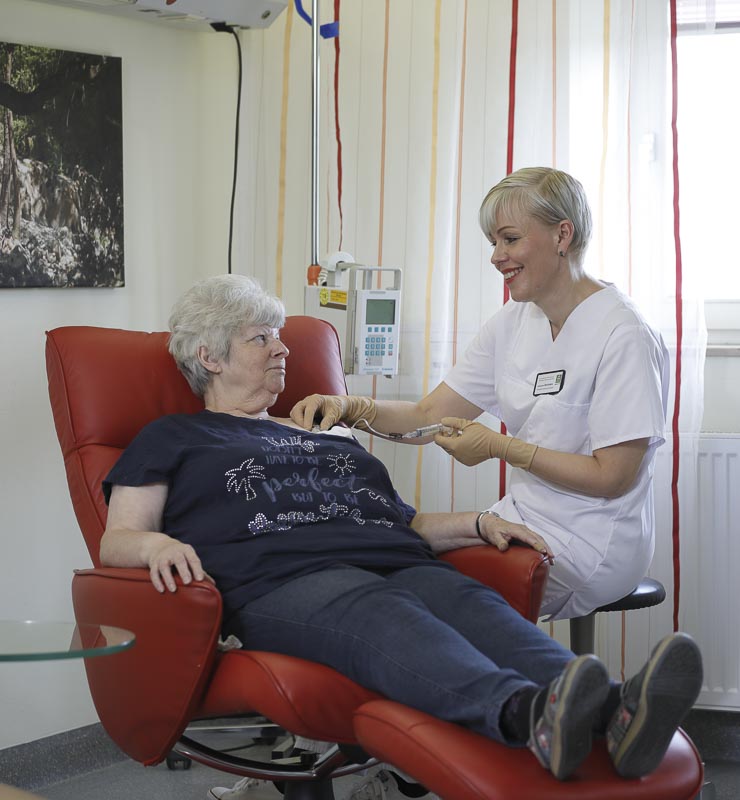Eine Frau im Medizinstuhl wird von einer lächelnden Krankenschwester im weißen Kittel behandelt.