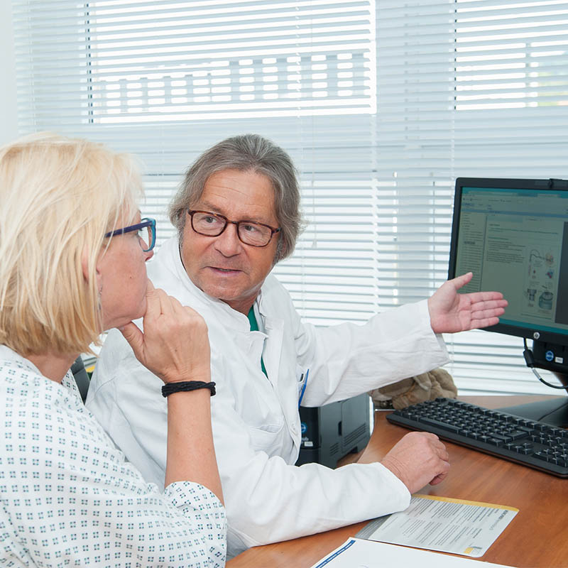 Ein Arzt erklärt einer Patientin etwas auf einem Computerbildschirm in einem Büro.