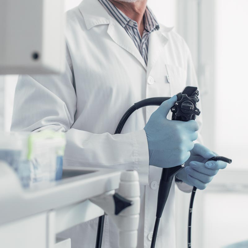 Ein Arzt in weißem Kittel hält ein Endoskop in einer medizinischen Umgebung.