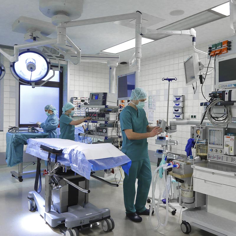 Ärzte in OP-Kleidung arbeiten in einem modern ausgestatteten Operationssaal mit medizinischen Geräten.