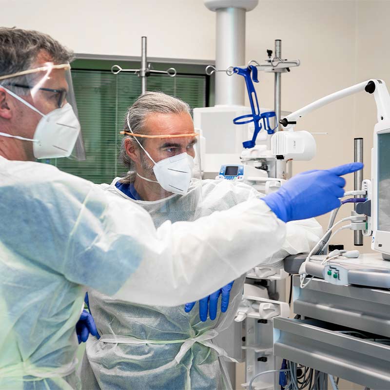 Zwei Ärzte in Schutzkleidung betrachten und diskutieren ein medizinisches Gerät im Krankenhaus.