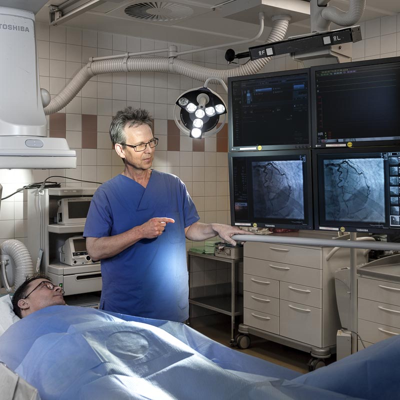 Ein Arzt im Operationssaal mit Patient, untersucht Röntgenbilder auf Monitoren.