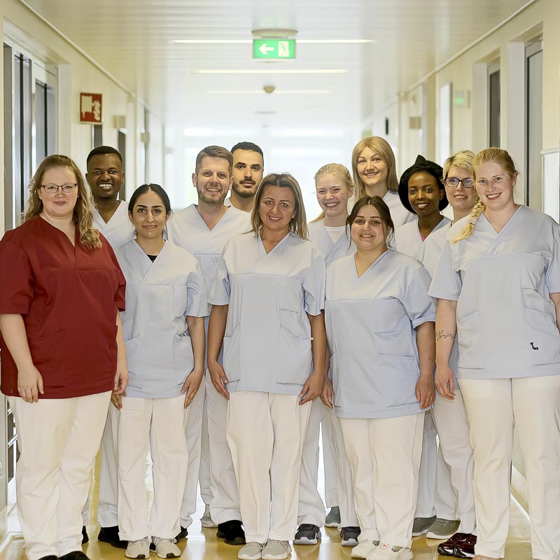 Eine Gruppe von Menschen in medizinischer Kleidung steht in einem Flur und lächelt in die Kamera.