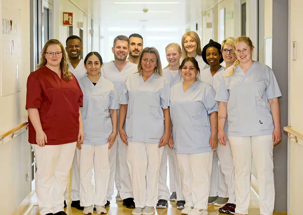 Eine Gruppe medizinischer Mitarbeiter in Kitteln steht gemeinsam in einem Flur eines Krankenhauses oder einer Klinik.