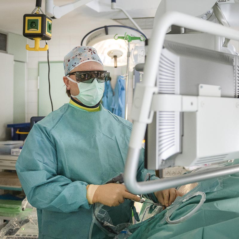 Ein Chirurg mit Schutzkleidung und -brille arbeitet im OP-Saal an einem medizinischen Gerät.