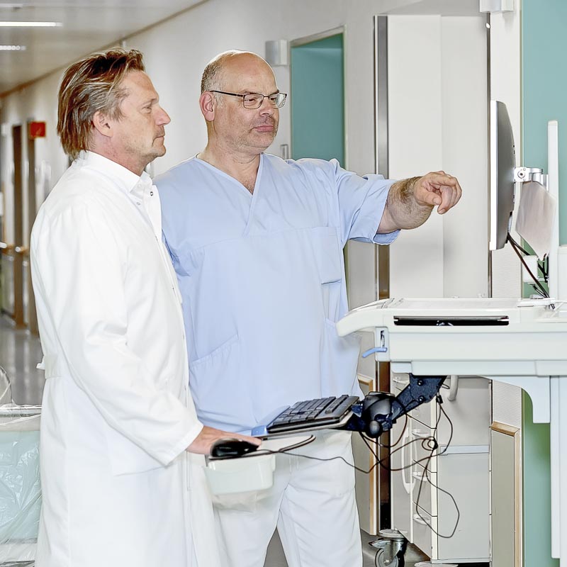 Zwei Ärzte in einem Flur, die auf einen Bildschirm schauen und diskutieren.